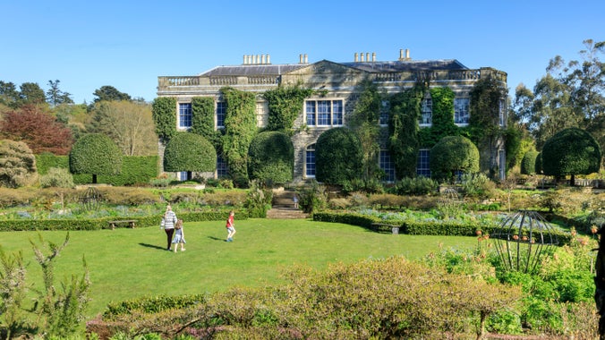 A family walking across the garden lawn surrounded by flower beds and hedges at Mount Stewart, with a view of the house in the background